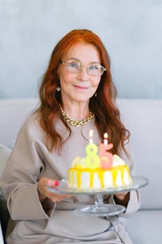 Elderly woman holding birthday cake with 85 candles, smiling indoors.